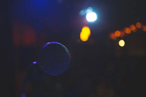 the microphone on the stage was shot at close range in an unusual purple-blue color. the room is dark. the lights of the bokeh-effect spotlights Shine pleasantly into the camera. there is no one in front of the microphone.