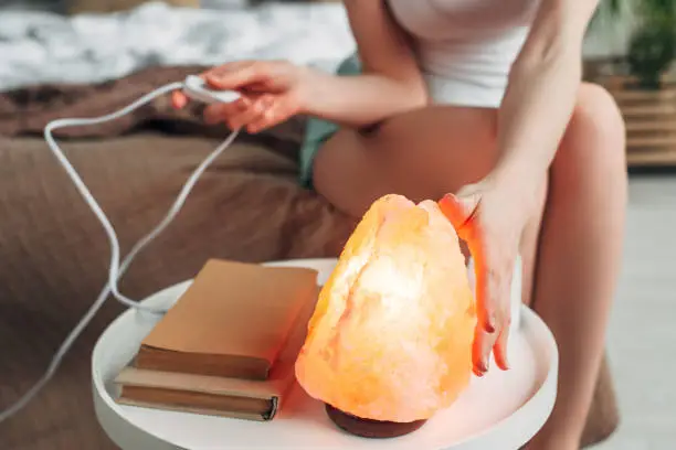 cropped view of young woman switching Himalayan salt lamp in bedroom with books