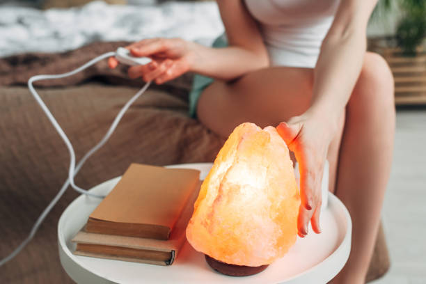 cropped view of young woman switching himalayan salt lamp in bedroom with books - pink salt imagens e fotografias de stock