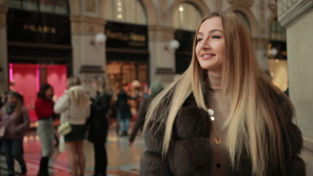 Blonde Woman In Expensive Fur Walks Along Shopping Center With Purpose Shopping,