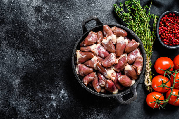 Raw chicken hearts in a pan. Organic offal. Black background. Top view. Copy space