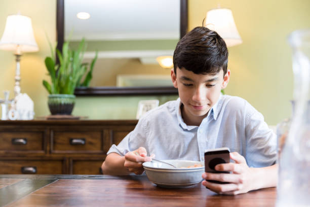 istock While eating breakfast alone, teen boy surfs net on phone 1224983555