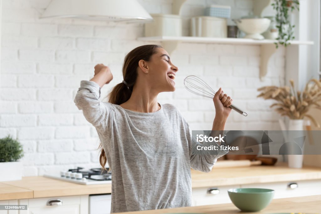 Excited funny girl singing into whisk, having fun in kitchen Excited funny girl singing into whisk, having fun in modern kitchen at home, happy girl holding beater as microphone, dancing, listening to music, having fun with kitchenware, preparing breakfast Women Stock Photo