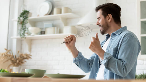 istock Funny handsome man singing into whist, having fun in kitchen 1224986919