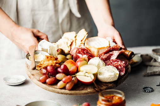 Midsection of woman holding fresh meze platter. Close-up of Mediterranean food. She is serving meal on table.