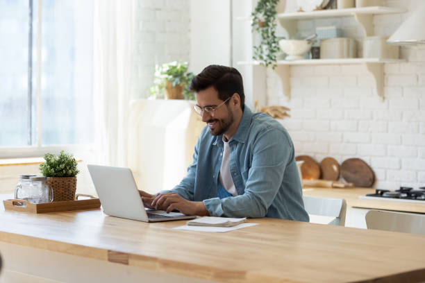 istock Smiling young man working on laptop in modern kitchen 1224987506