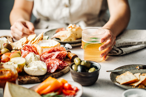 Woman taking cheese from plate with different appetizers on grey table, closeup