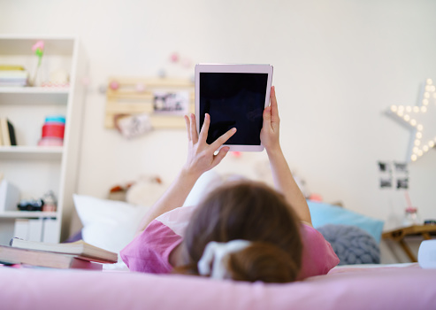 Rear view of young girl with tablet on bed, relaxing during quarantine. Copy space.