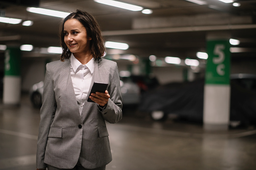 Businesswoman in garage unlocking car and using phone