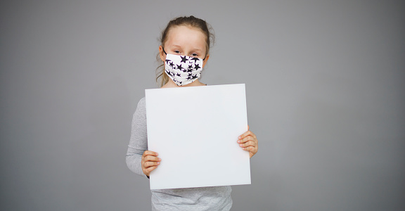 girl with message board and nose mouth mask is posing in front of grey background