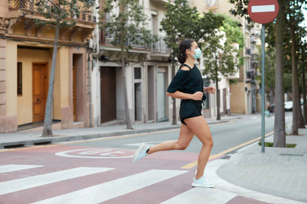 una giovane donna che fa jogging per strada con una maschera protettiva. - general practice foto e immagini stock