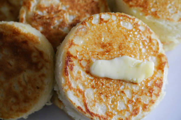 Close-up image of stack of freshly baked, homemade buttered crumpets on china plate, melting butter, home baking concept Stock photo showing a plate containing a pile of freshly baked, warm, homemade buttered crumpets with melting butter. crumpets stock pictures, royalty-free photos & images
