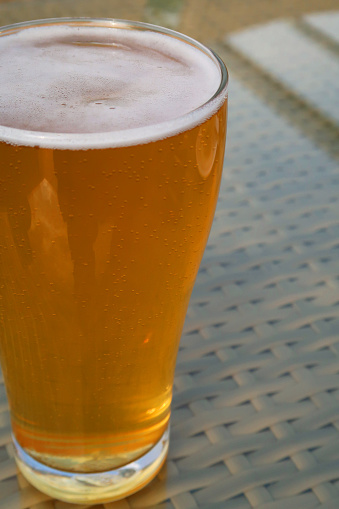 Stock photo showing glass pint of alcohol, beer, cider or lager, with a frothy head of bubbles. Taken in a pub beer garden.