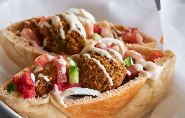 Authentic fresh falafels balls inside of two halves of pita bread sandwich with chopped salad and drizzle of tahini sauce on top, close-up of chickpea falafel in a gluten-free pita Close-up of chickpea falafel in a gluten-free pita lebanese culture stock pictures, royalty-free photos & images