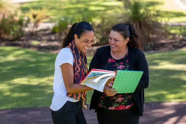Young aboriginal student talking to her tutor outdoors in the sun in Australia.