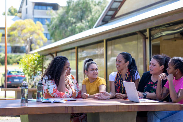 Sitting Together Group of young female aboriginal students sitting with their tutor outdoors in the sun in Australia. aborigine woman stock pictures, royalty-free photos & images