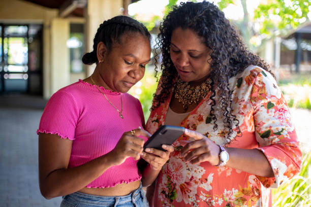 Leisure Time Two young aboriginal female students looking at a smart phone together. aborigine woman stock pictures, royalty-free photos & images