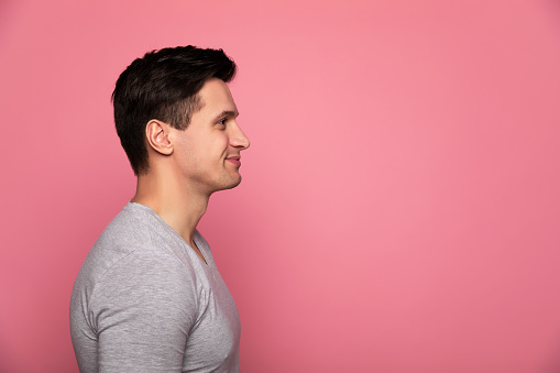 Handsome man. Close-up photo of an attractive man in a grey t-shirt, who is standing in profile and smiling.