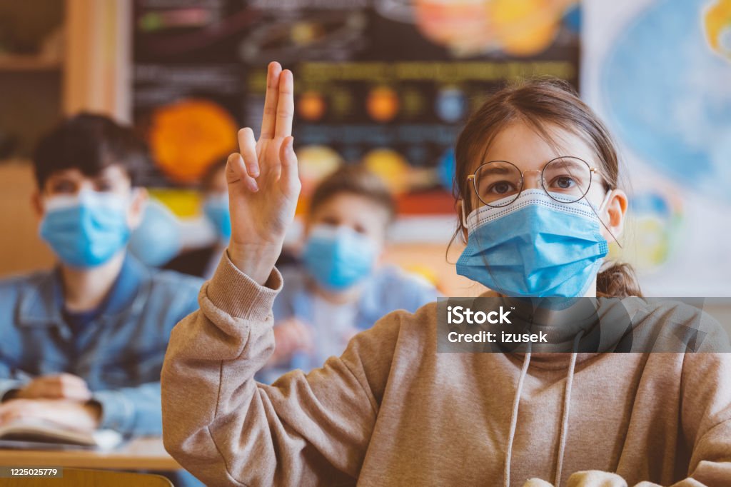 High school students at school, wearing N95 Face masks. High school students at school, wearing N95 Face masks. Sitting in a classroom and listening to teacher. Teen girl is rising hand. Protective Face Mask Stock Photo