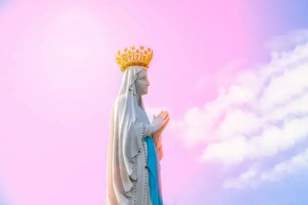Virgin Mary statue on the pink sky background. Statue of Our Lady, fragment. Lourdes, France, Hautes Pyrenes