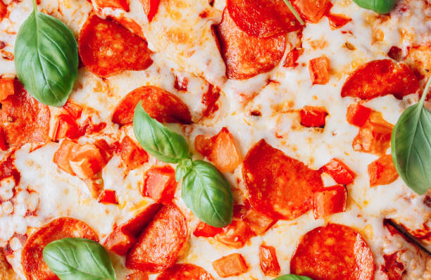 A seamless food texture. Appetizing background pepperoni pizza with basil closeup filling the frame.