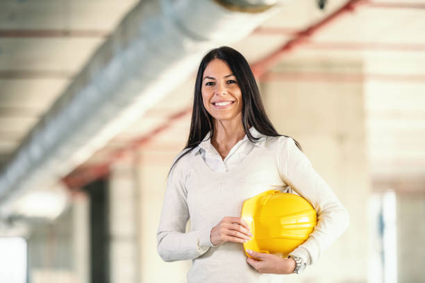 istock Young smiling female architect standing at construction site and holding helmet under armpit. 1225026942
