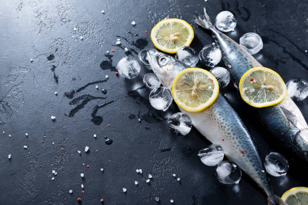 istock 2 fresh raw fish mackerel, lemon slices, ice cubes, spices, salt on a black background top view 1225028039