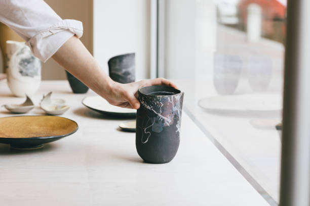 Hand of unrecognisable woman gallerist putting artisan's ceramic vase at shop window.