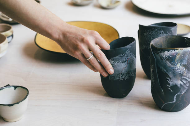 Hand of unrecognisable woman gallerist putting artisan's ceramic vase at shop window.