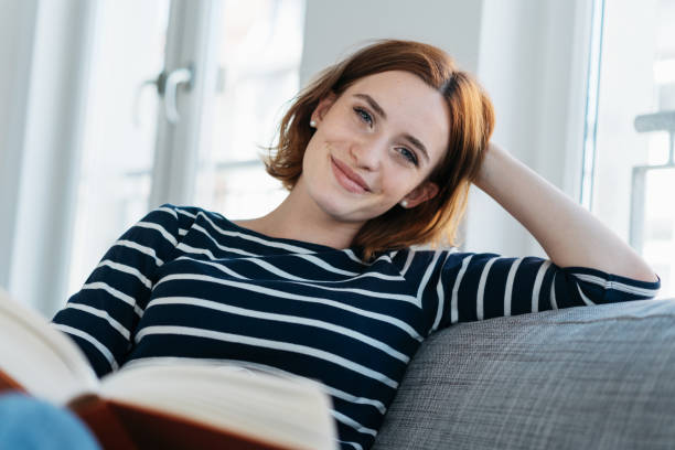 mulher bonita jovem relaxando em um sofá em casa - resting relaxation book break - fotografias e filmes do acervo