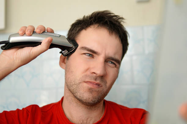 a man cuts his hair on his head with an electric razor. suffering from cutting hair. clean yourself up on your own. - unwillingness imagens e fotografias de stock