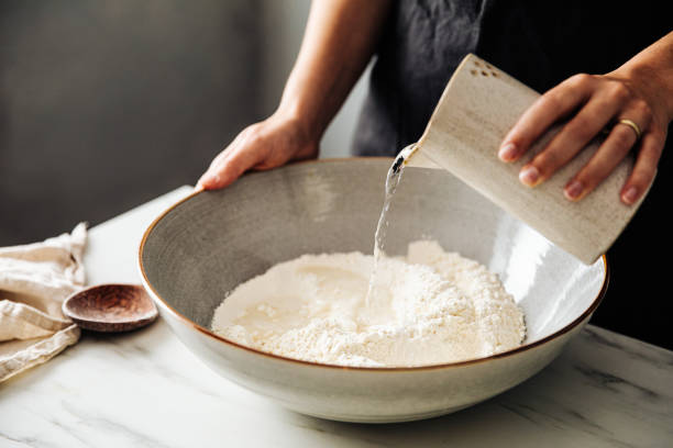 Woman pouring water on rye and wheat flour in bowl Midsection of woman pouring water on rye and wheat flour in bowl. Female is standing in kitchen. She is preparing sourdough bread. flour photos stock pictures, royalty-free photos & images