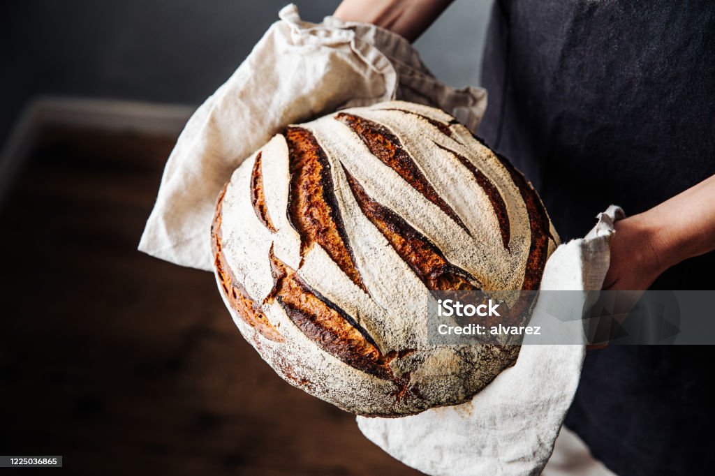 Woman holding fresh baked sourdough bread Close-up of fresh baked sourdough bread. Woman is holding wheat and rye beard. She is in kitchen. Bread Stock Photo
