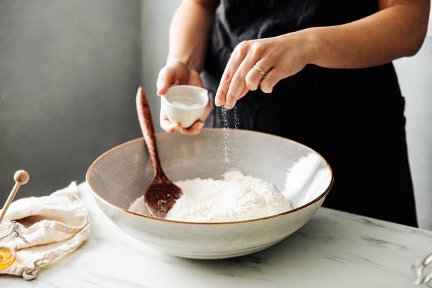 donna che cosparge sale nella farina prima della miscelazione - sale da cucina foto e immagini stock