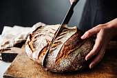 Woman cutting sourdough bread with knife on board