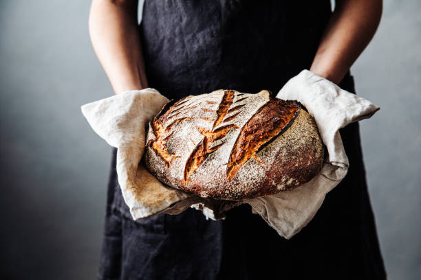 Woman with fresh baked sourdough bread in kitchen Midsection of woman holding fresh baked sourdough bread. Close-up of homemade wheat and rye beard. She is in kitchen. loaf of bread stock pictures, royalty-free photos & images