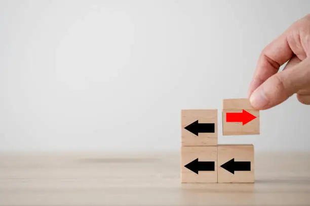 Photo of Hand putting red arrow on wooden cube which opposite direction with black arrow. Disruption and different thinking for discovery new technology  and new business opportunity concept.
