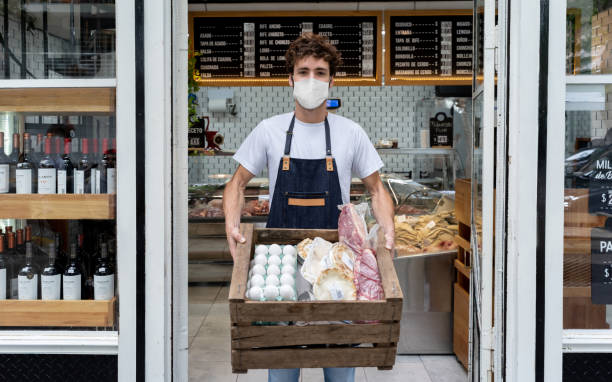 istock Man working at a deli preping delivery orders for customers and wearing a facemask 1225040487