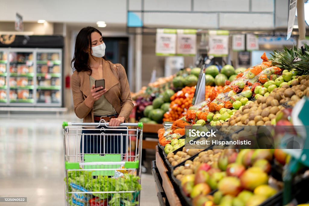 Donna che fa shopping al negozio di alimentari indossando una maschera facciale - Foto stock royalty-free di Supermercato
