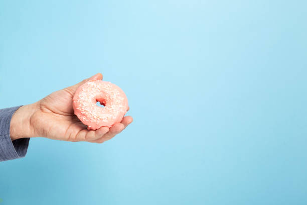 istock Men 's hand holds donut with pink icing and coconut pastry topping, blue background. Copy space 1225040571