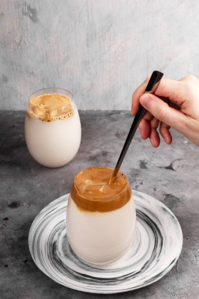 istock Popular drink Korean Dalgon coffee. Long spoon mixes whipped foam from soluble coffee, sugar and hot water with milk in glass on grey background 1225041833