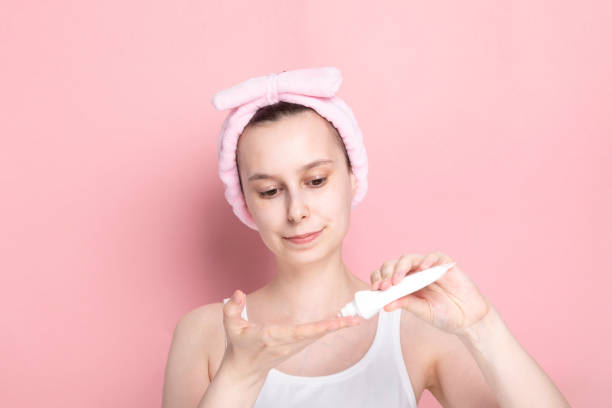 istock Young girl without makeup apply face moisturizer lotion on pink background 1225044891