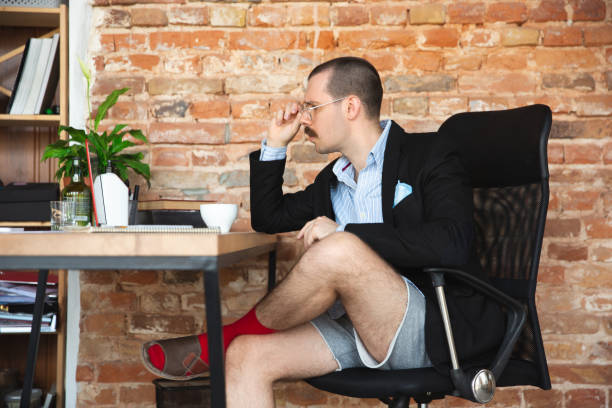 молодой человек без штанов, но в куртке работает на компьютере, ноутбуке. удаленный офис во время коронавируса, веселая и комфортная работа  - men underwear naked business стоковые фото и изображения