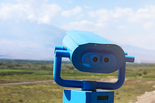 Blue tourist telescope with green field and cloudy sky view.