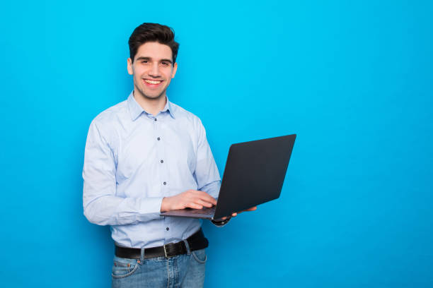 istock Happy young man working on laptop on blue background 1225054408