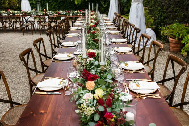 in backyard of villa in Tuscany there is banquet wooden table decorated with cotton and eucalyptus compositions, glasses, candles and plates are placed on table