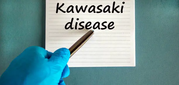 Male doctors hand in blue glove, words 'kawasaki disease' on a white note. Beautiful blue background.