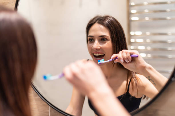 istock Young woman looking in mirror while brushing teeth, dental hygiene 1225060072