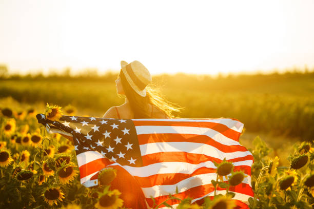 Patriotic girl  in hat with the American flag in a sunflower field at sunset.  Fourth of July. Freedom. Patriotic girl  in hat with the American flag in a sunflower field at sunset.  Fourth of July. Freedom. american flag flowers stock pictures, royalty-free photos & images