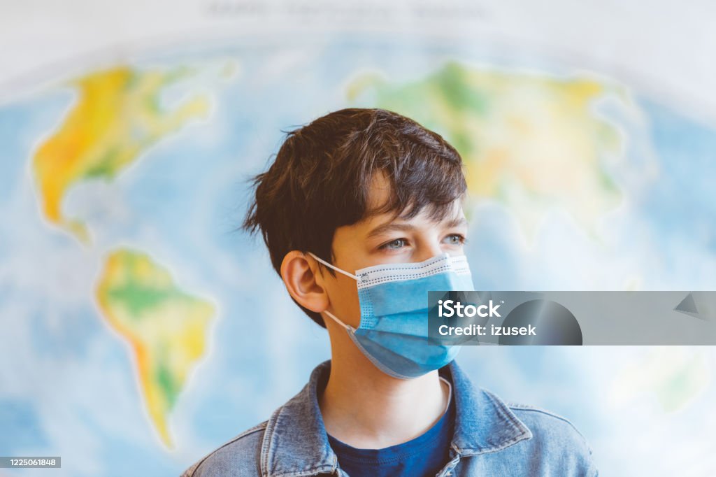 High school students at school, wearing N95 Face masks. A 13-year-old teenager wearing a N95 Face masks is standing in front of a world map Education Stock Photo